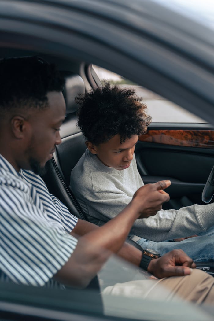 A father and son sit in a car, focusing on driving lessons inside the vehicle.